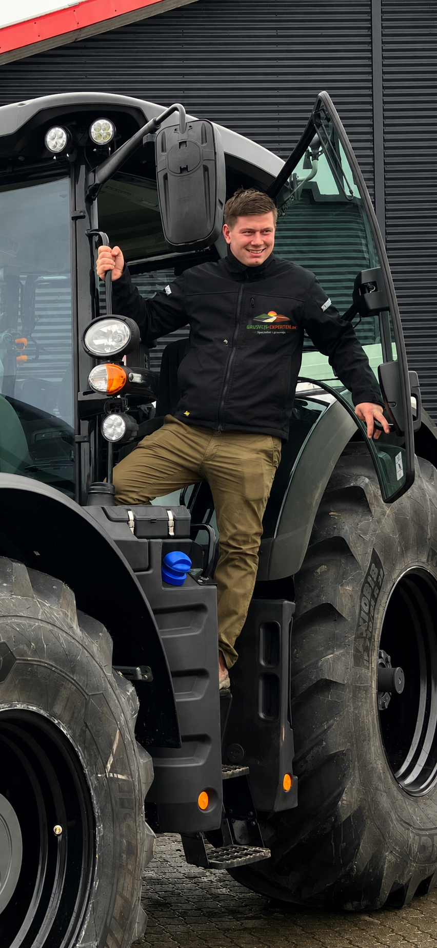 Christopher Leisted — grundlægger af Grusvejs-Experten — står på sin traktor i firma-jakke